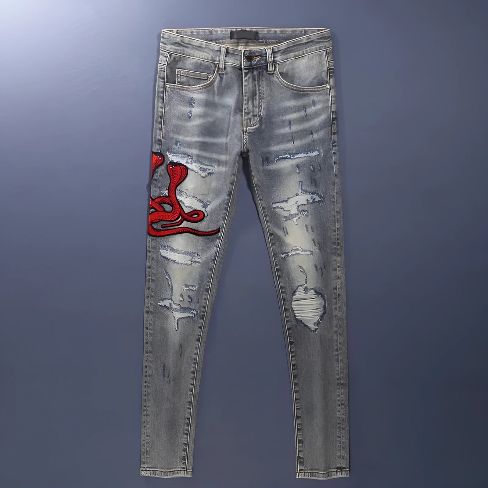 Close-up of distressed slim fit jeans showing worn wash, hole patches, and embroidery on blue denim.