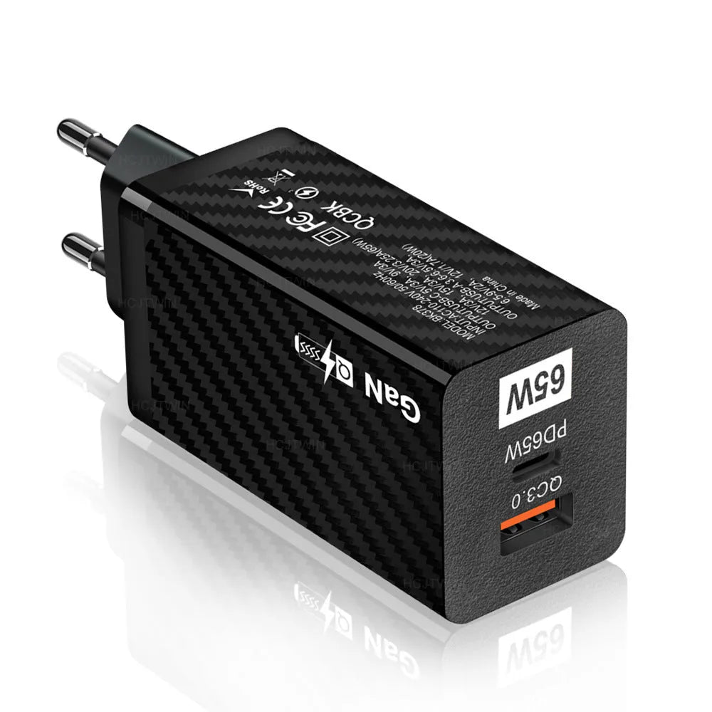 White GaN 65W USB-C fast charger plug with UK, EU, and US attachments on a desk.