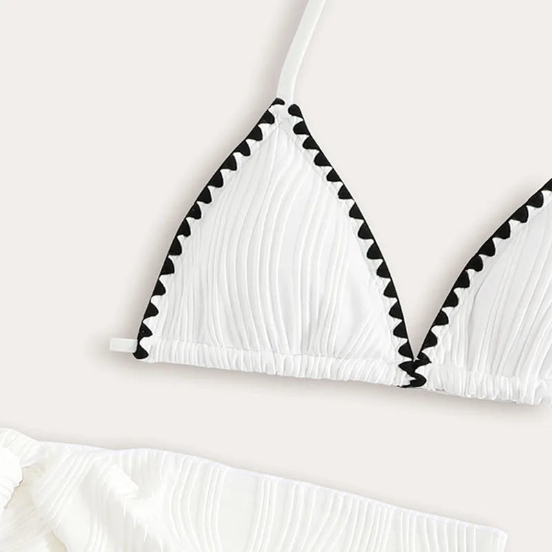 Solid white three-piece girls swimsuit set with top, pants, and skirt on a beach setting.
