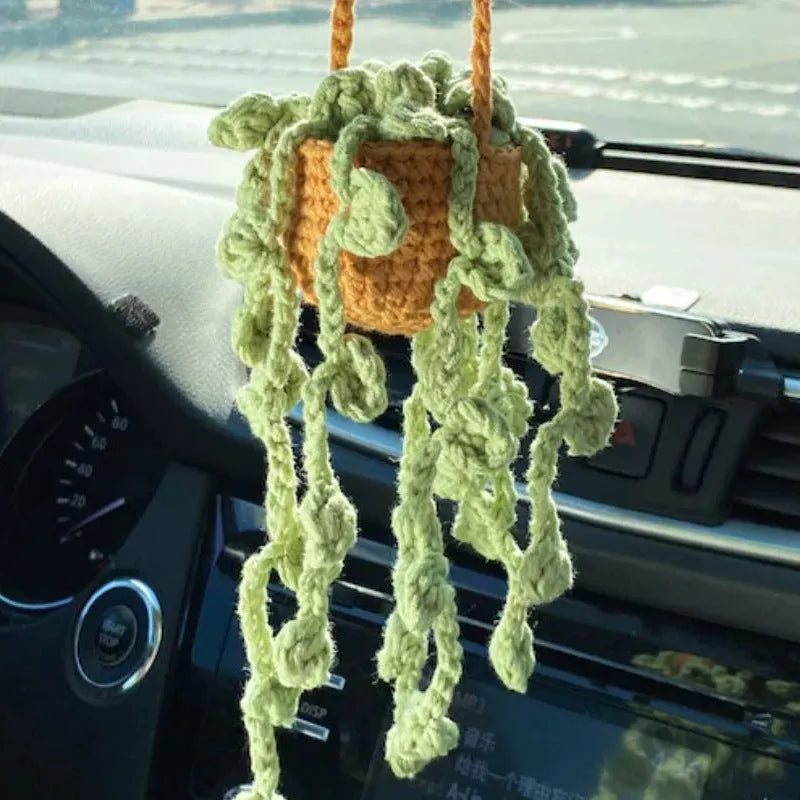 Green and white crocheted car plant decoration with hanging rope on a car dashboard.