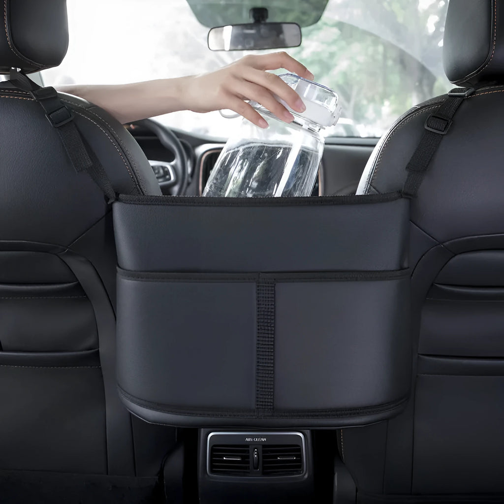 Black leather car seat storage bag with carbon fibre pattern, shown between vehicle front seats.