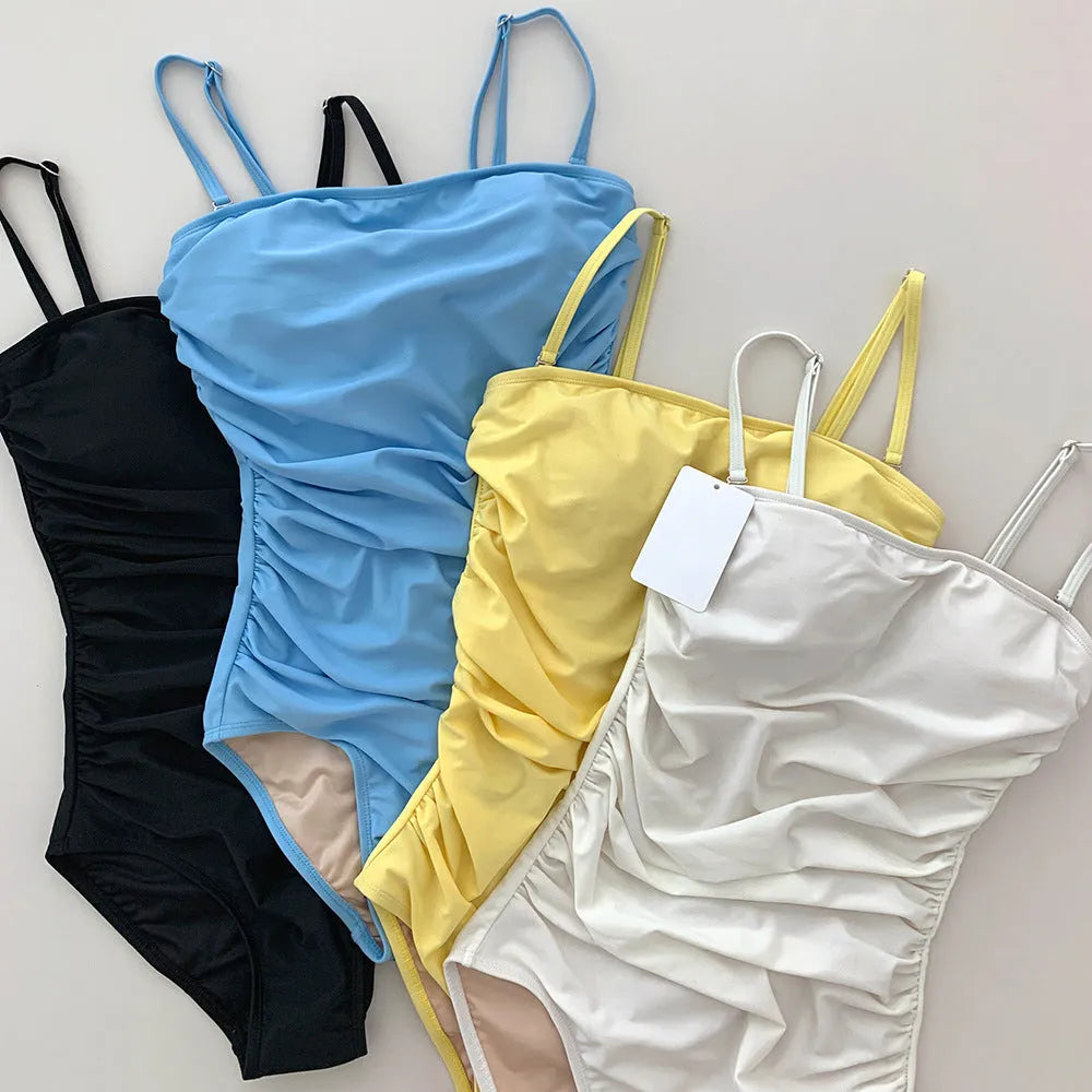 Sling top one-piece swimsuit with belly pleats in blue, shown on a model.