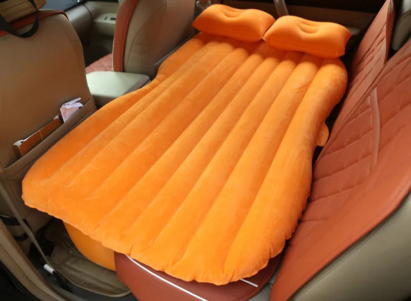 Inflatable car bed with flocked surface folded beside storage bag and two pillows