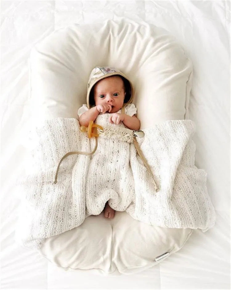 Beige portable baby nest crib cot for newborns on a neutral background.