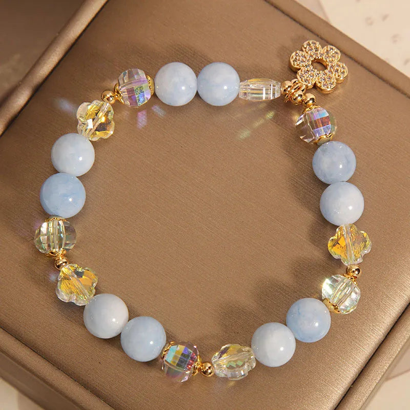 Aquamarine crystal bracelet with four-leaf clover charm and pearl detail on a wrist.