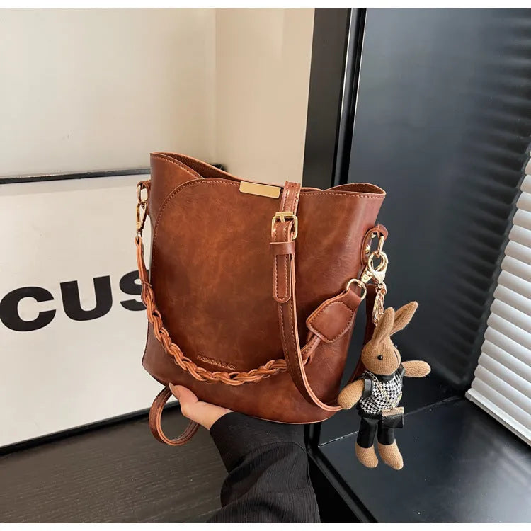 Women's retro PU messenger bag in brown with compact bucket shape, pendant, and double shoulder strap connector