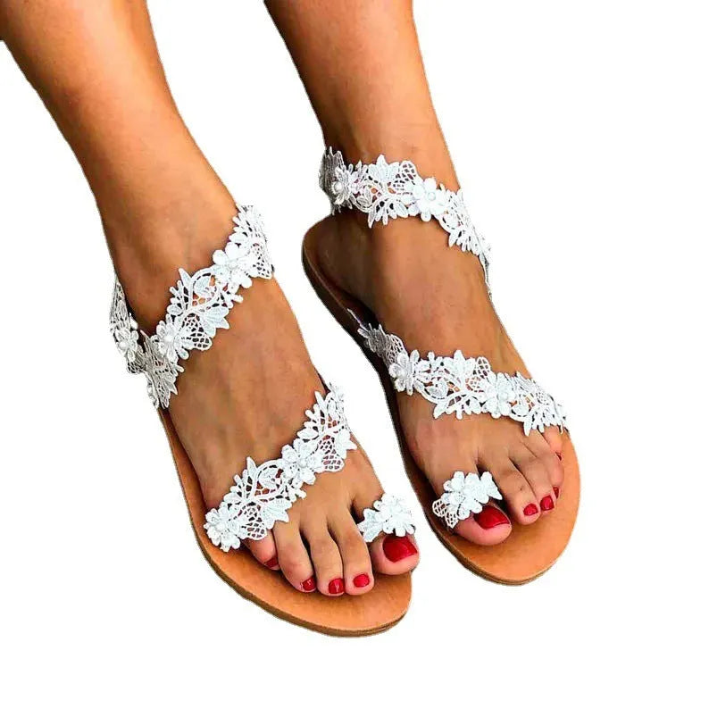 White flat sandals with rhinestone floral decoration on patent leather, showing backless slip-on design