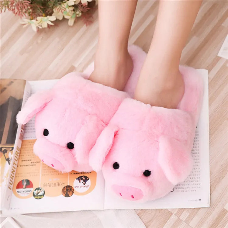 Pink pig-shaped plush floor slippers on a clean floor, showing the short plush fabric and pig design details.