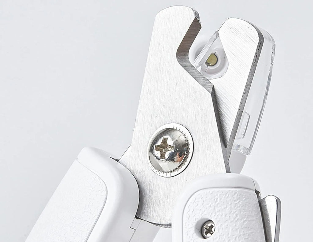 White pet nail clippers with LED light, transparent guard, and a nail file on a table