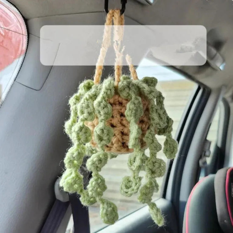 Green and white crocheted car plant decoration with hanging rope on a car dashboard.