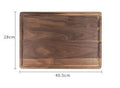 Black walnut wood cutting board with sauce groove and carved side handle on kitchen counter