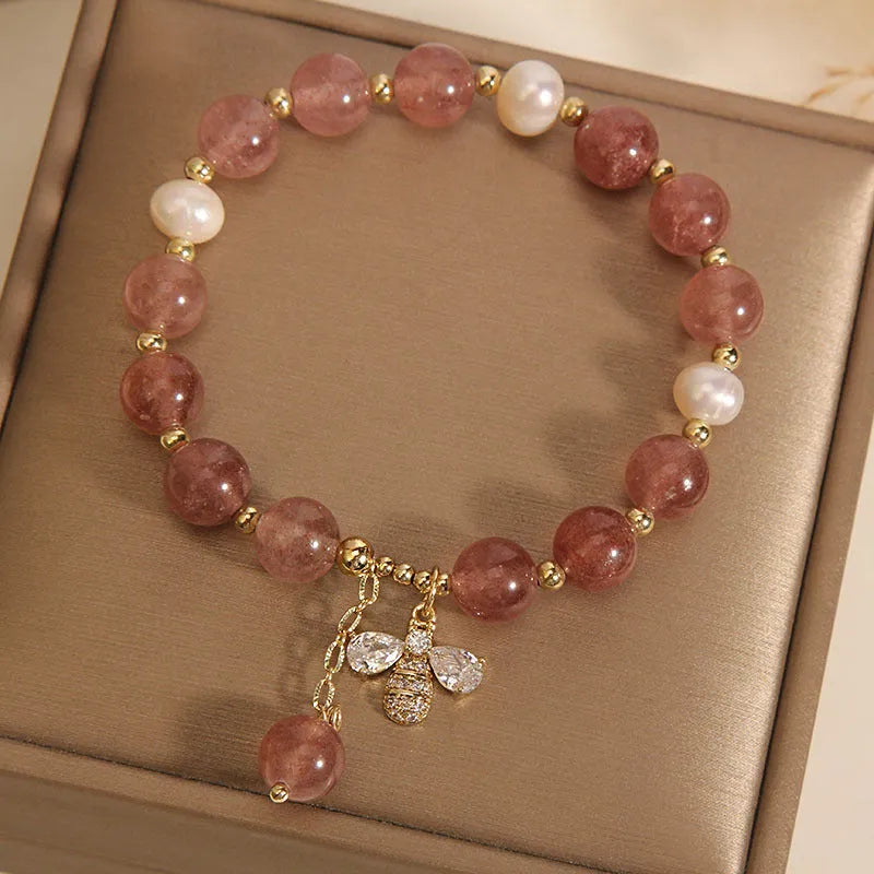 Women's pink strawberry quartz and white freshwater pearl bracelet with zircon details on wrist.