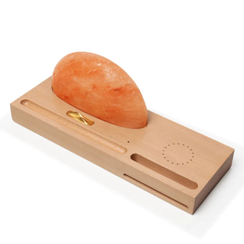 Wooden-based table lamp with a glowing orange Himalayan salt shade, wirelessly charging a mobile phone on its surface.
