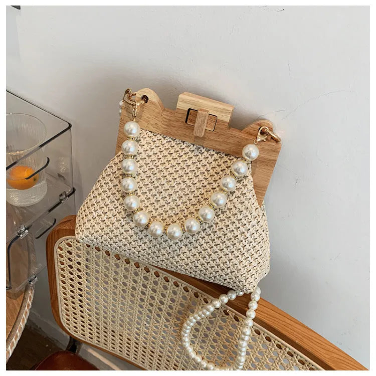 Women's horizontal square straw shoulder bag with pearl chain strap, shown in beige colour with visible sewing line detail.