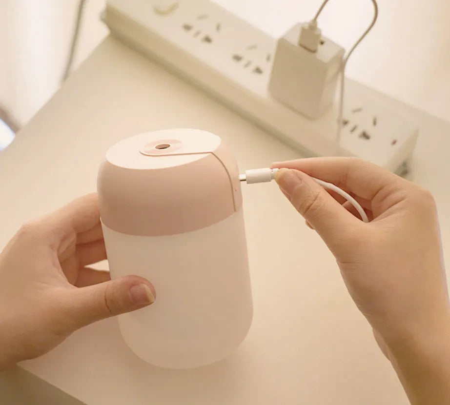 White cylindrical mini USB aromatherapy humidifier on a desk with charging cable.