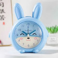 Pink and blue cartoon children's alarm clock with night light on a bedside table