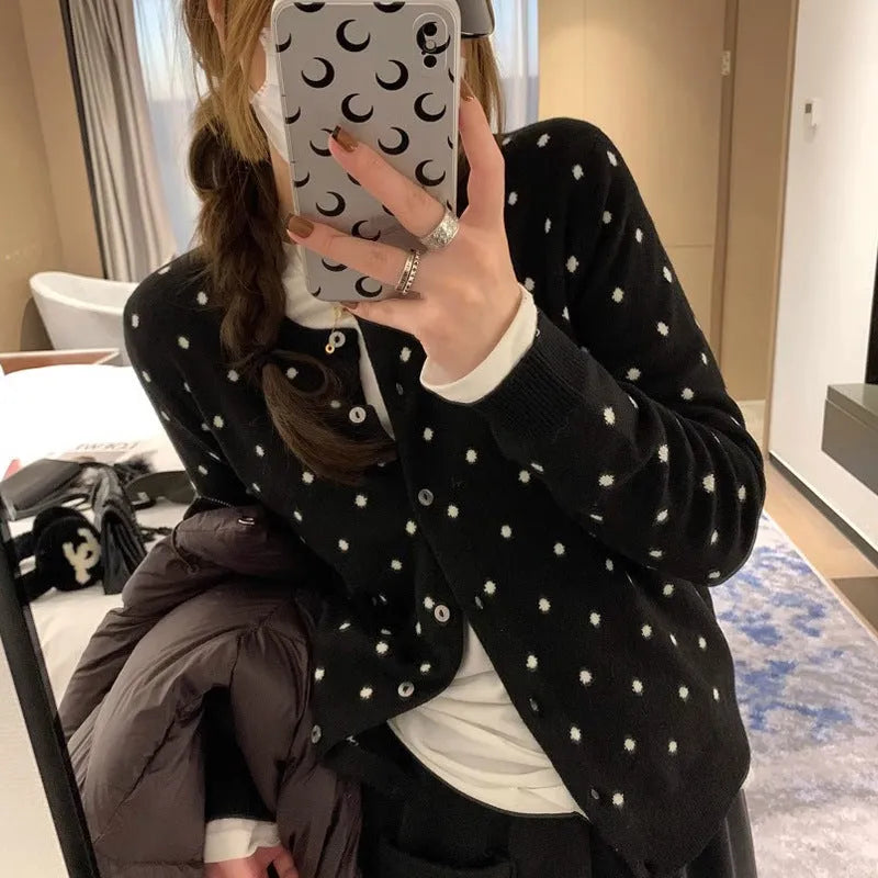 Women's grey dot pattern knitted cardigan with crocheted flower detail on a mannequin.