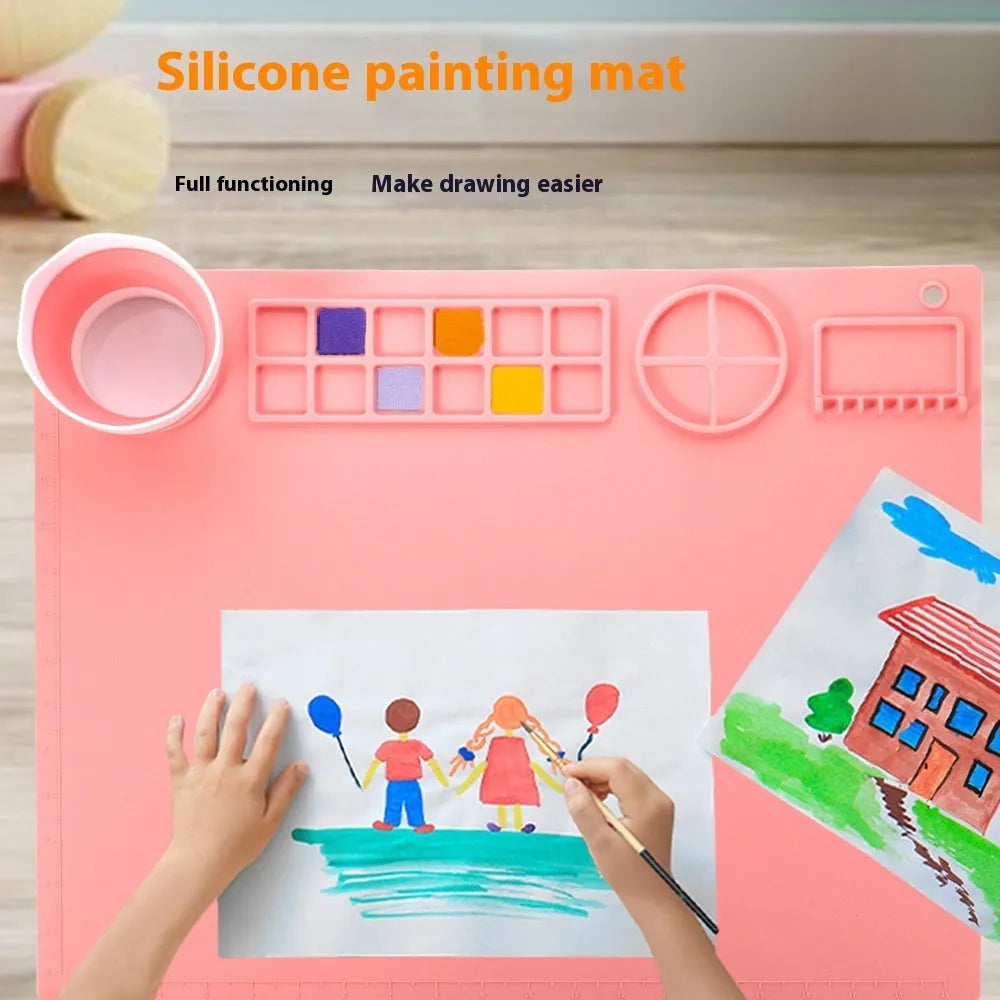 Light blue silicone painting mat with two round mixing bowls, placed on a wooden table with paintbrushes.