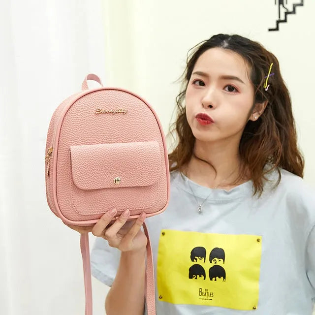Small black women's backpack shoulder bag with zipper closure shown next to a mobile phone for scale