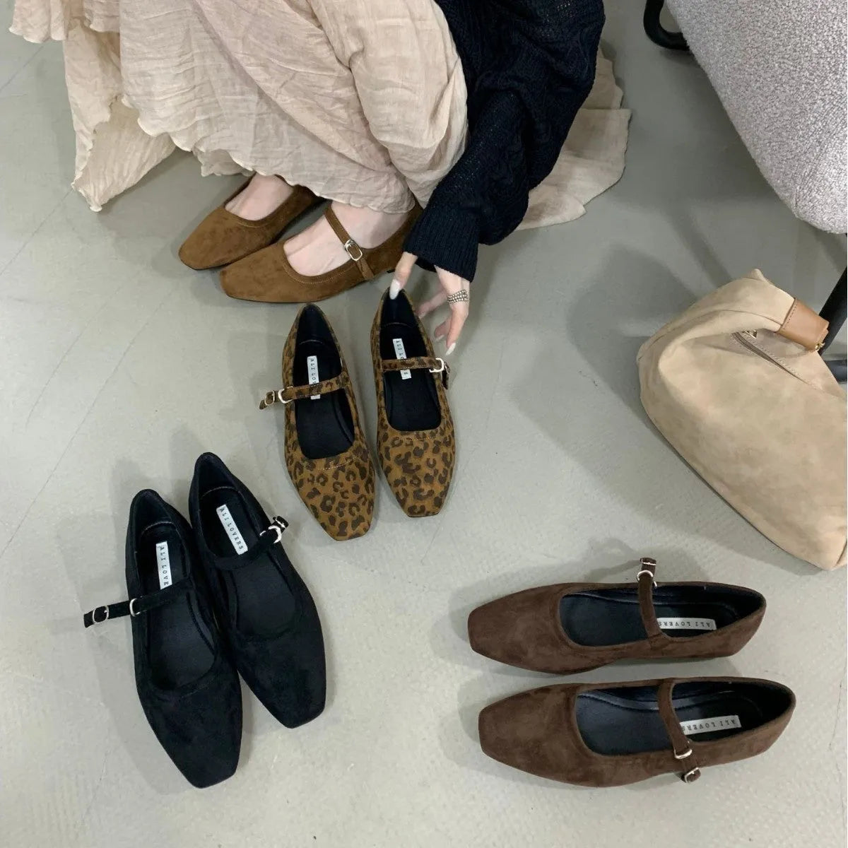 Women's black suede flat shoes with buckle closure and low heel on a neutral background
