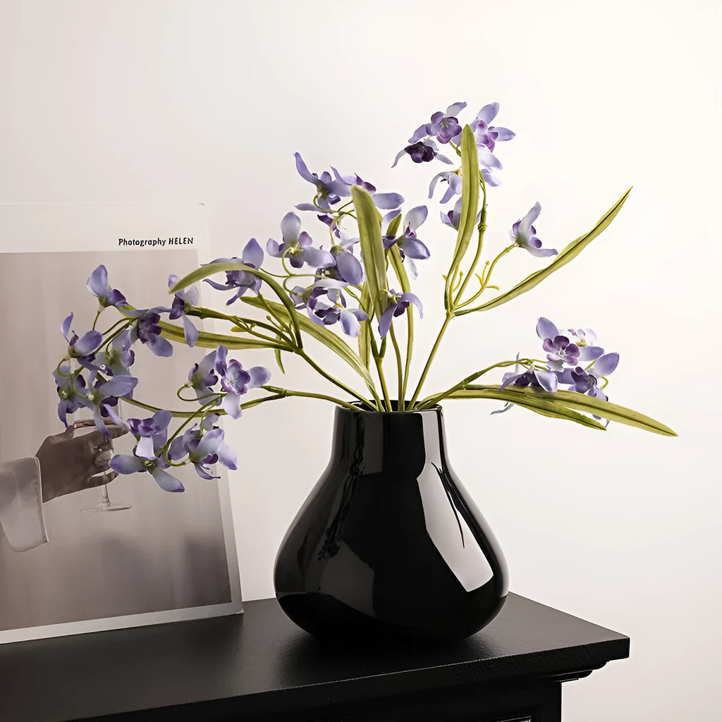 Black ceramic vase with round belly shape and two white flower ornaments arranged decoratively