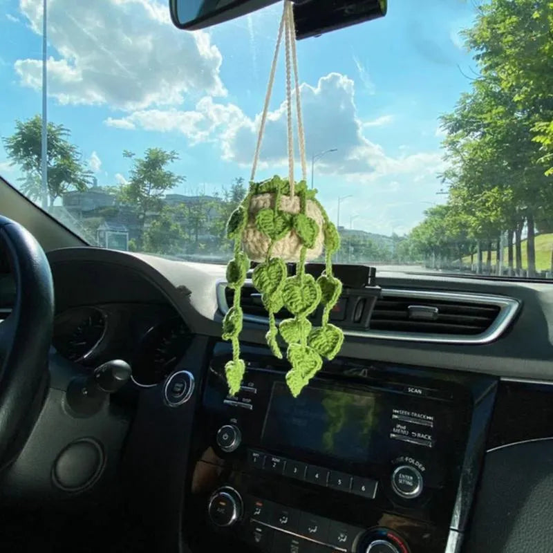 Green and white crocheted car plant decoration with hanging rope on a car dashboard.