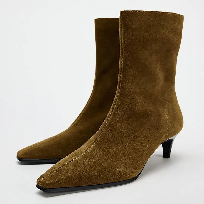 Brown square toe ankle boots with a side zipper and pointed stiletto heel on a wooden floor.