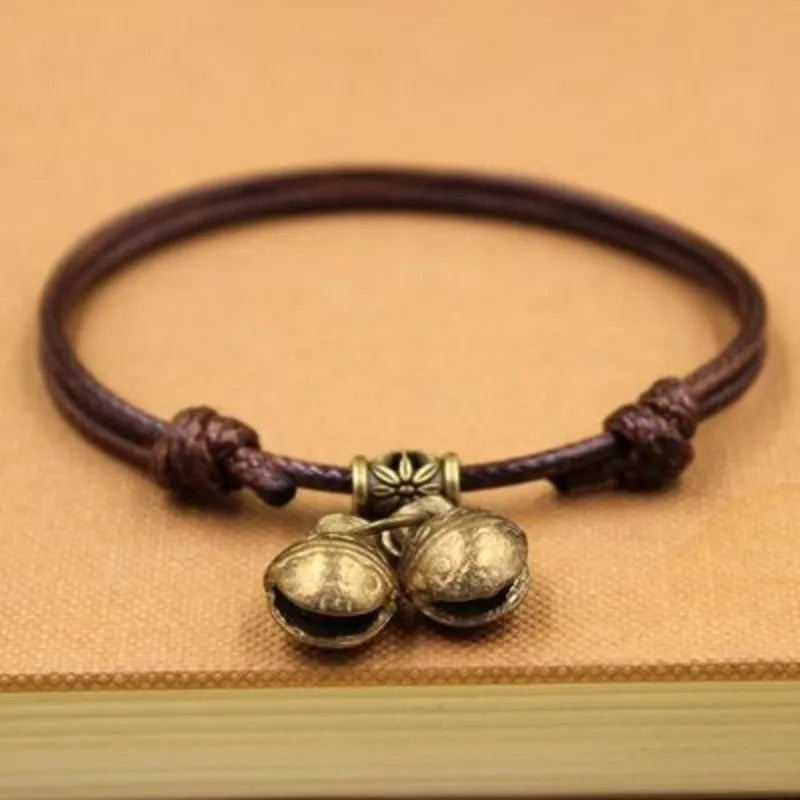 Black nylon rope dog collar with a small brass bell on a wooden background.