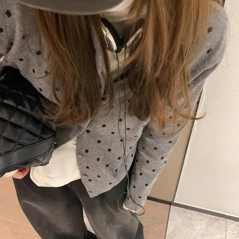 Women's grey dot pattern knitted cardigan with crocheted flower detail on a mannequin.