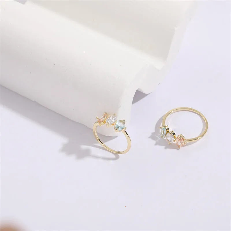 Gold colour geometric triangle ring with horse eye design and tricolour zircon stones on a white background