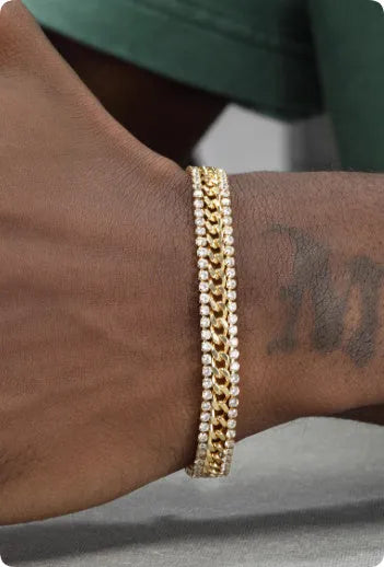 Gold coloured hip hop style tennis bracelet with chain links and artificial gemstone inlays on a wrist.