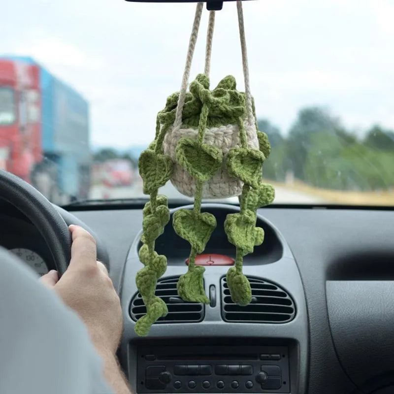 Green and white crocheted car plant decoration with hanging rope on a car dashboard.
