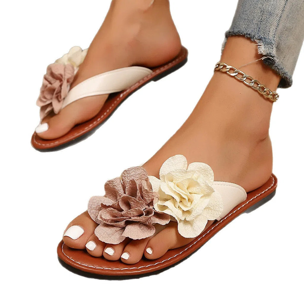 Beige flip flop open toe flat sandals with adjustable strap and two-way flower decoration on a beach setting