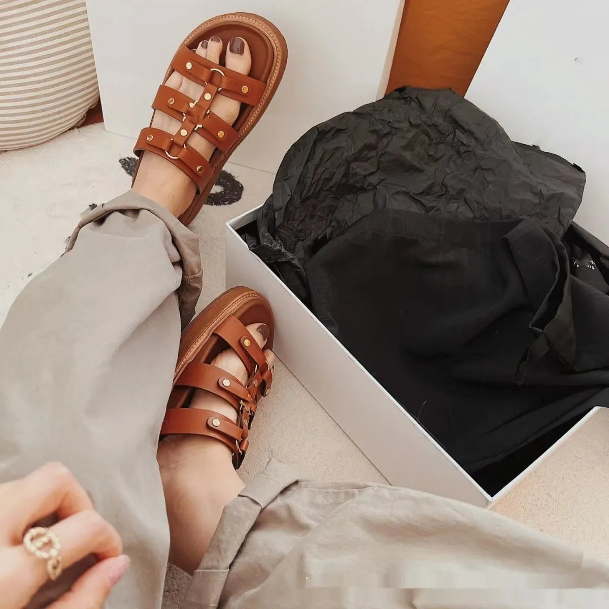 Women's brown retro Roman strap sandal slippers made from sheepskin and patent leather on a wooden floor.