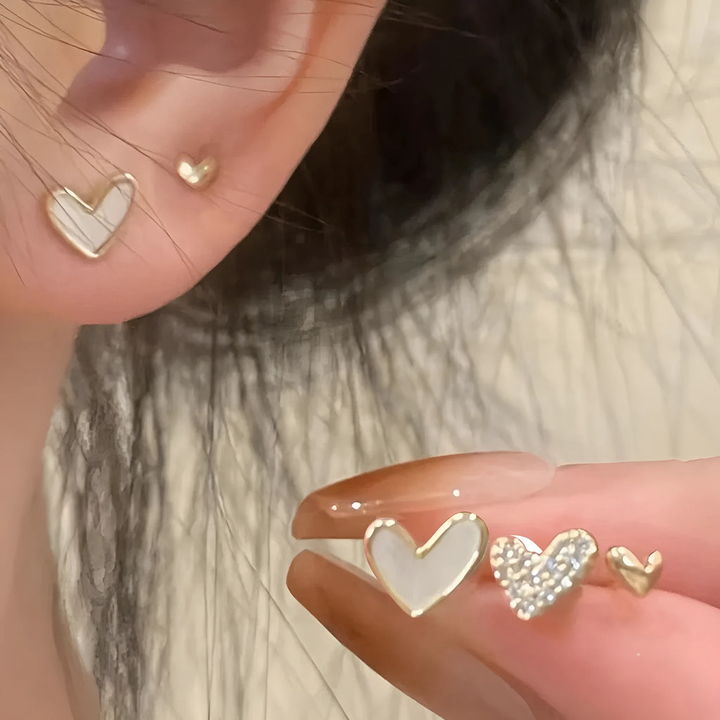 Three pairs of heart-shaped alloy earrings in gold, black, black and white, and pink colours with electroplated finish