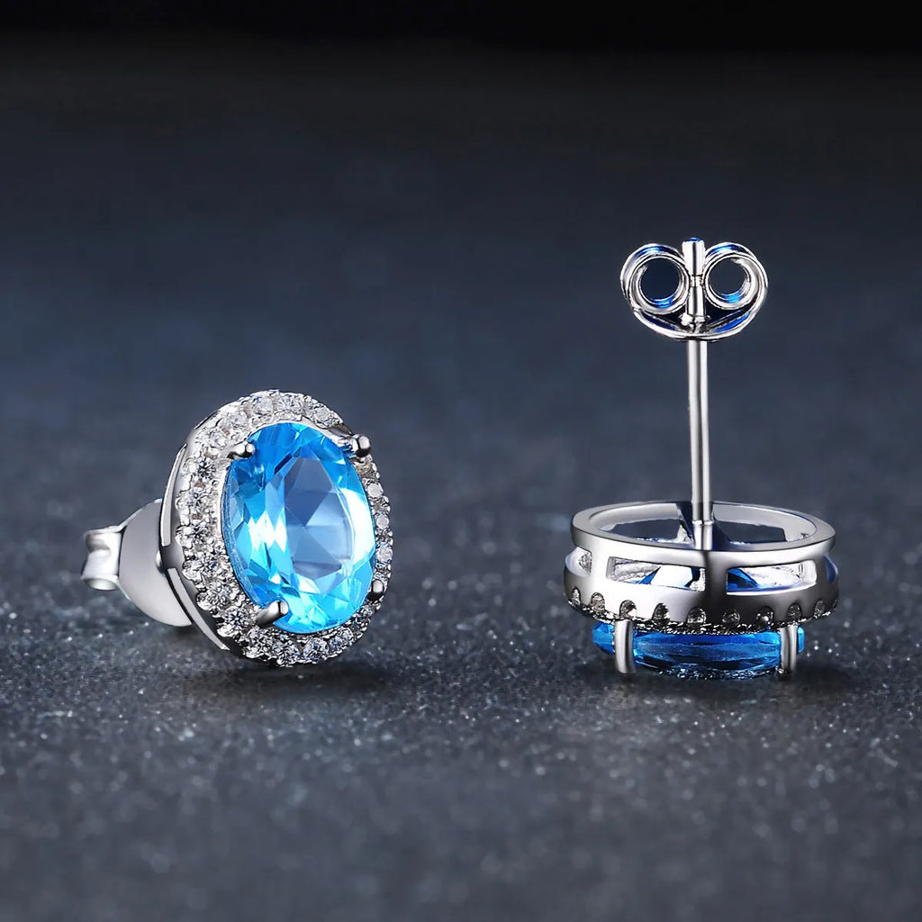 Women's sterling silver jewellery set with blue topaz stones, showing geometric earrings, necklace, ring, and pendant.