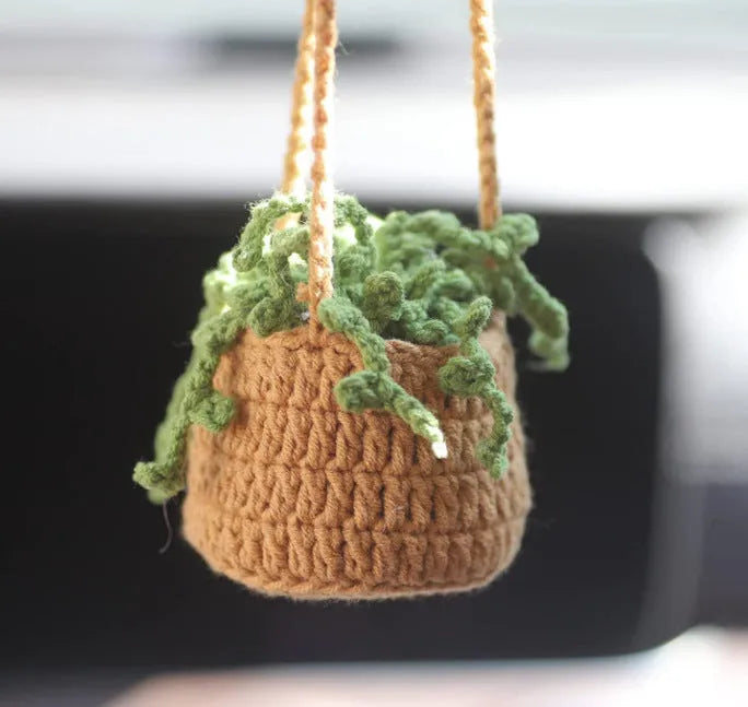 Green and white crocheted car plant decoration with hanging rope on a car dashboard.