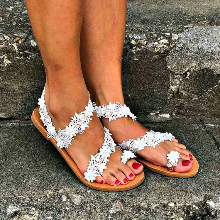 White flat sandals with rhinestone floral decoration on patent leather, showing backless slip-on design