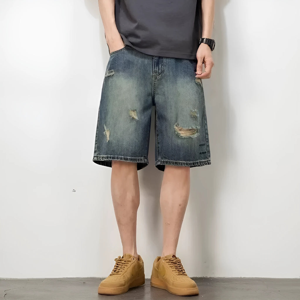 Blue men's distressed denim shorts with a loose, straight leg fit on a model.