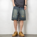 Blue men's distressed denim shorts with a loose, straight leg fit on a model.