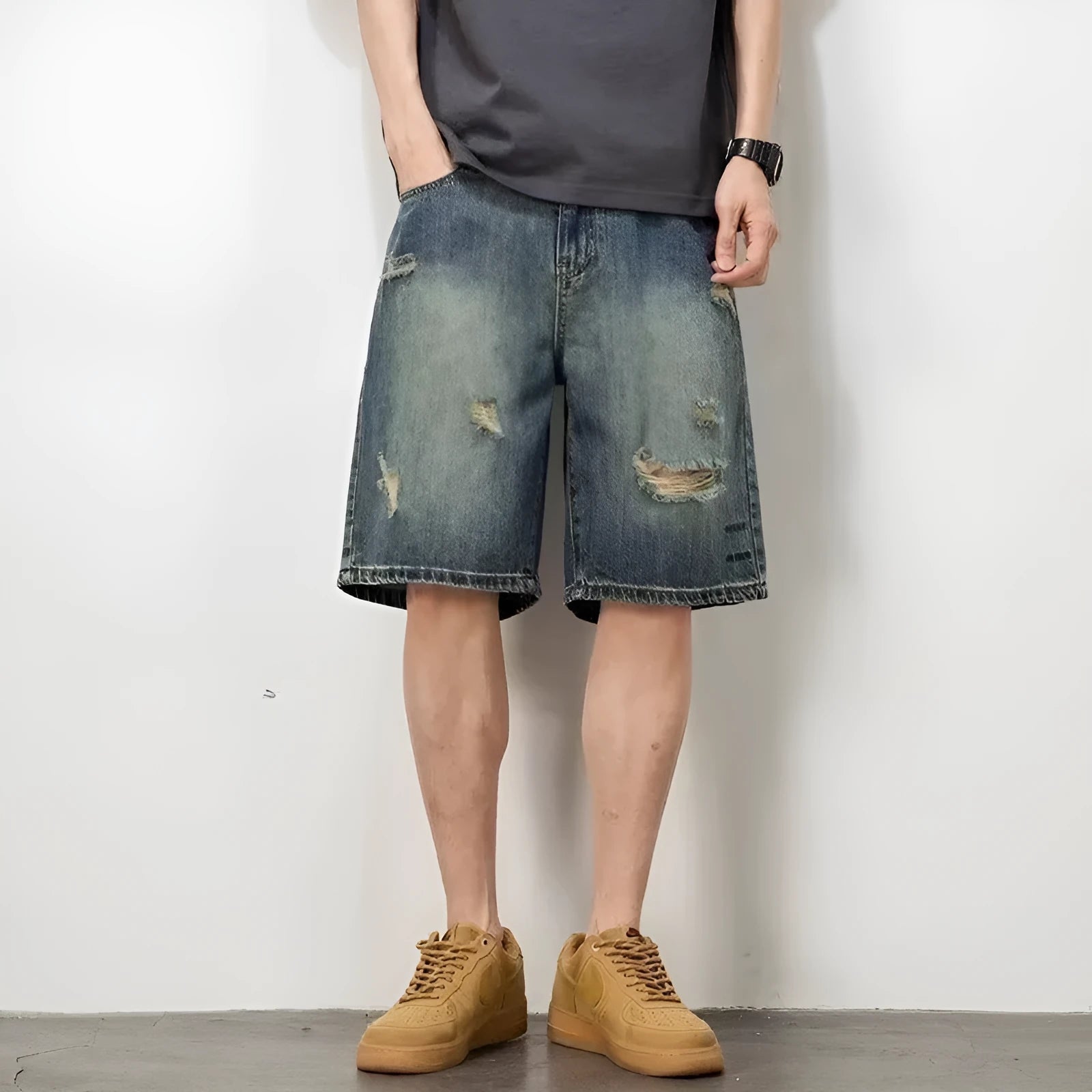 Blue men's distressed denim shorts with a loose, straight leg fit on a model.