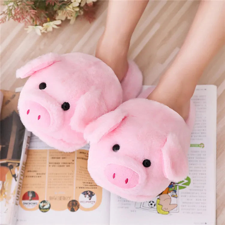Pink pig-shaped plush floor slippers on a clean floor, showing the short plush fabric and pig design details.