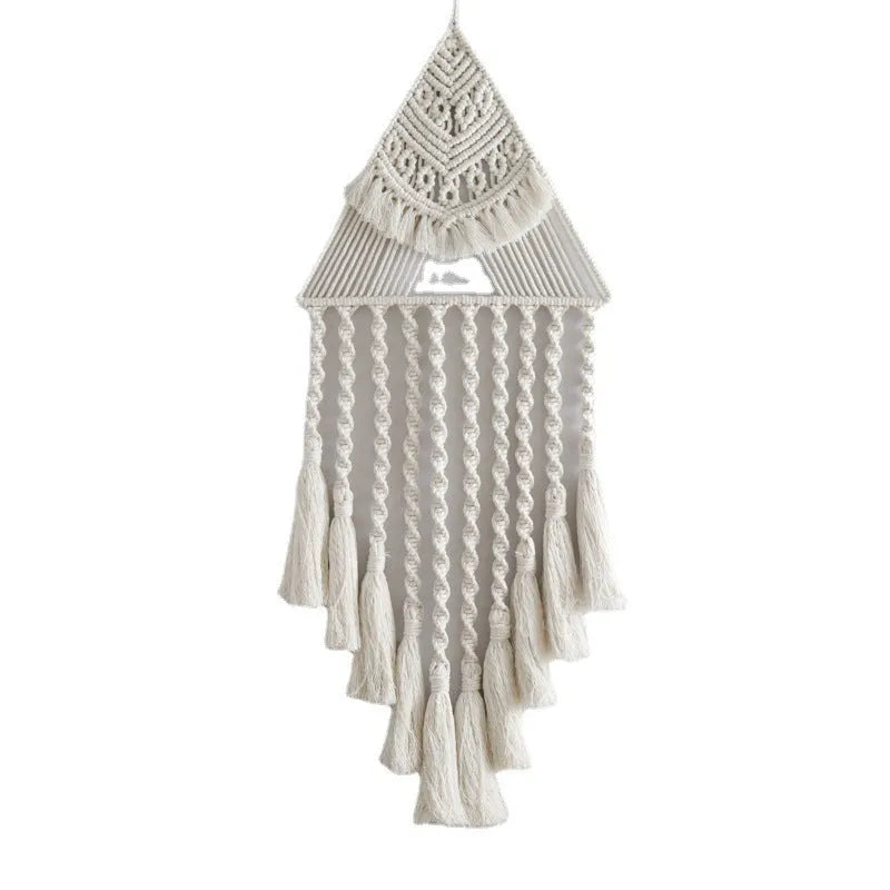 Handwoven triangle dream catcher pendant in brown with cotton web, iron ring, wooden beads, and tassel on a light wall