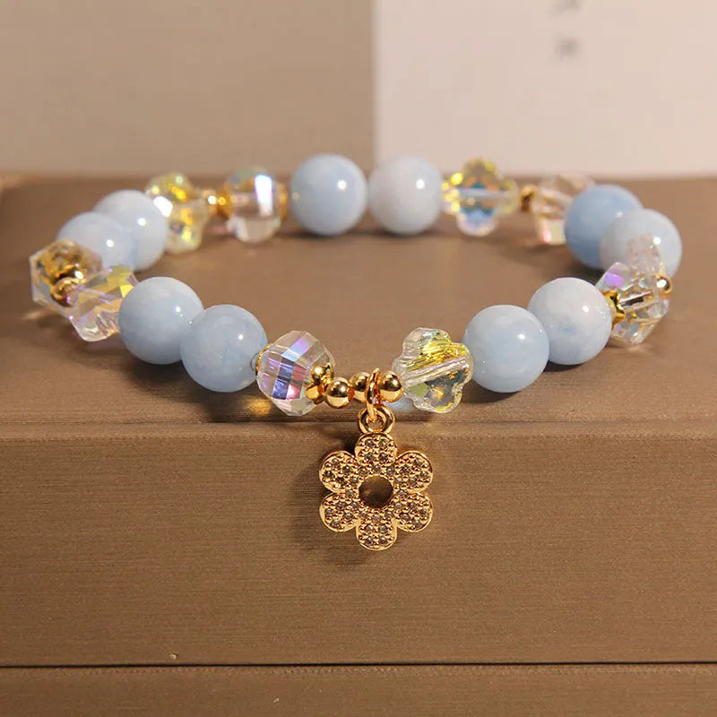 Aquamarine crystal bracelet with four-leaf clover charm and pearl detail on a wrist.