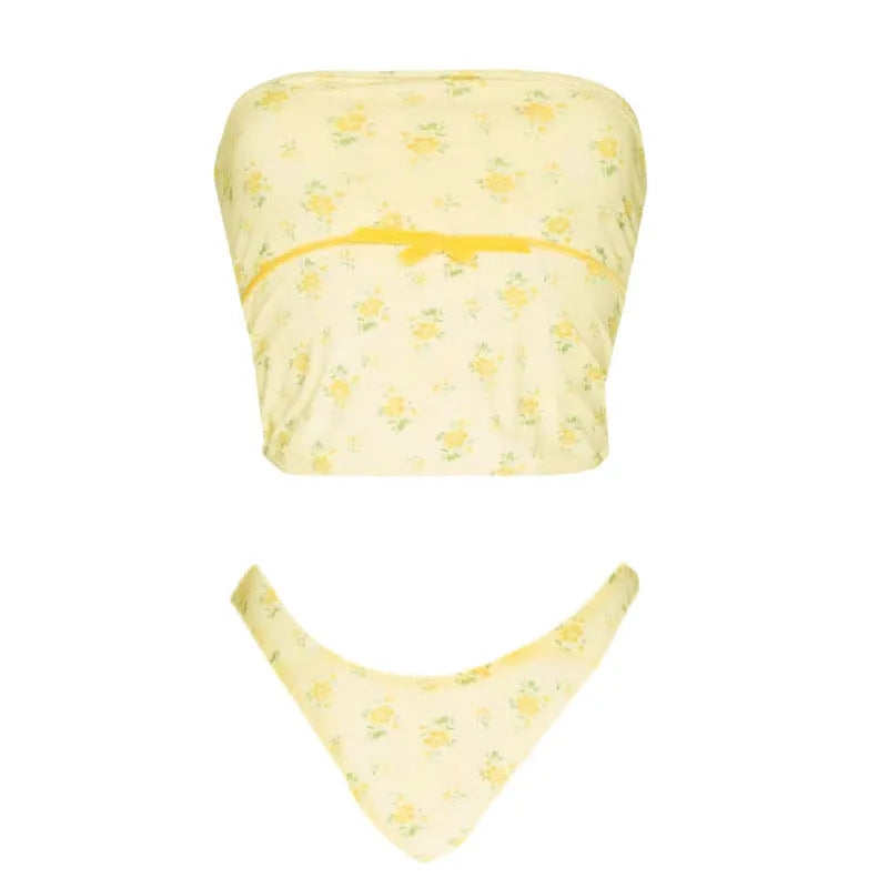 Bright yellow women's two-piece swimsuit with tube top, shorts, and flower pattern on beach