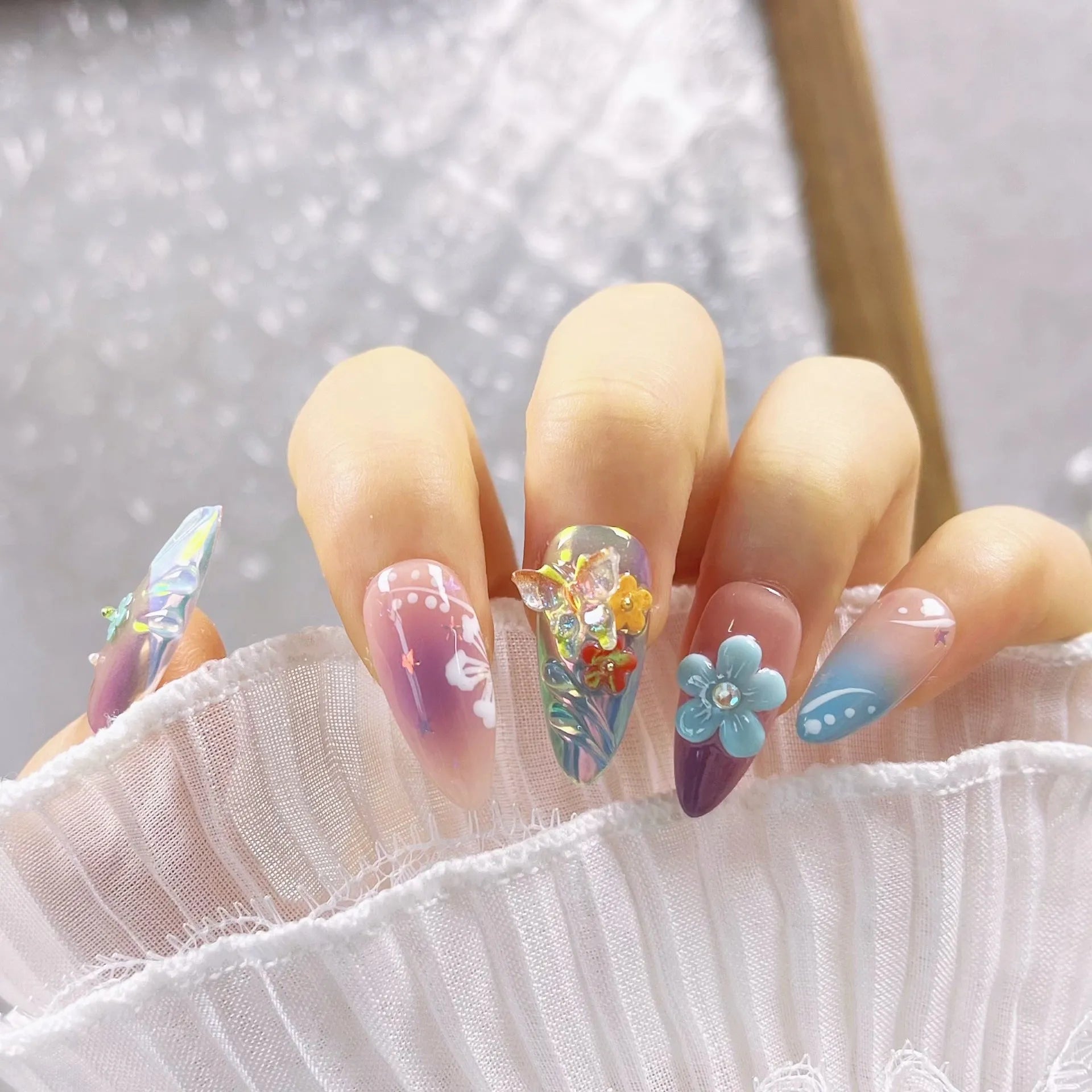 Handmade floral and butterfly nail art sculptures for manicure decoration in almond shape.