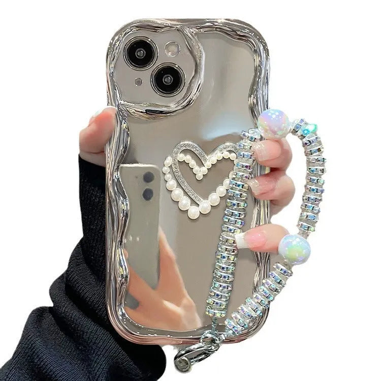 Silver grey silicone phone case for iPhone 15 Pro Max with three-dimensional pearls and chain, electroplated finish, and matching bracelet on a table