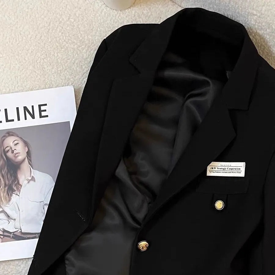 A women's black loose-fitting short suit coat with long sleeves and pockets.