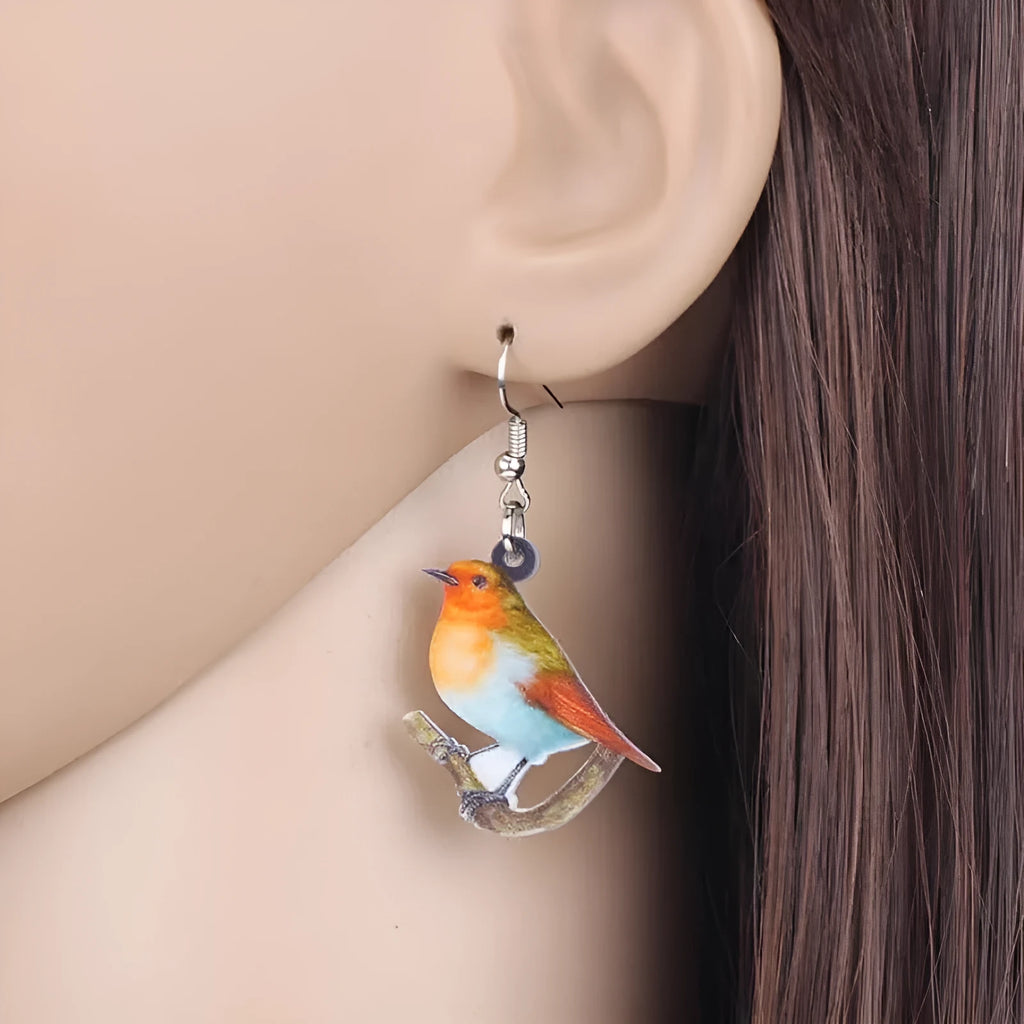 A pair of blue titmouse bird pendant earrings made from clear acrylic with geometric shapes and snake chain links.