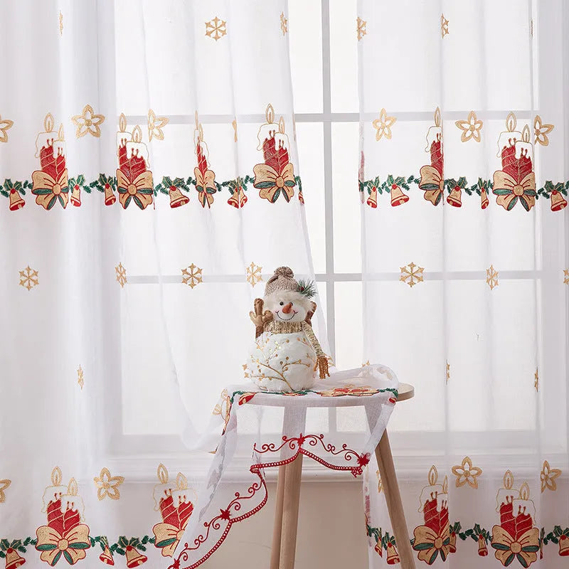 Pair of white Christmas curtains with red and green embroidered snowflakes, shown hanging in a window.